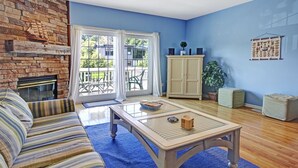 A living room with a sofa, a coffee table, a fireplace, a cabinet, and a view through the glass doors. - Water Street Townhouses (Saugatuck)