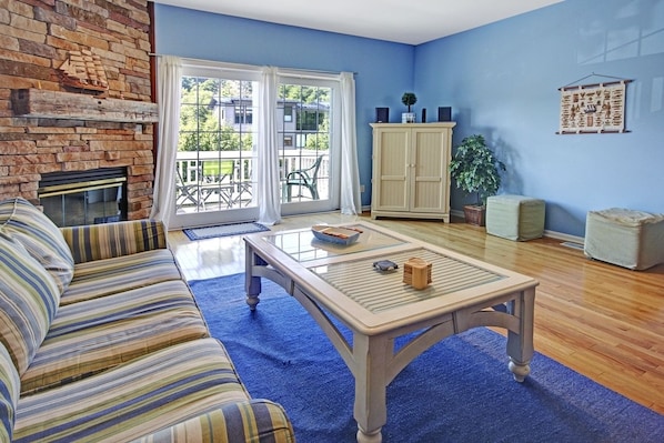 Una sala de estar con sofá, una mesa de centro, chimenea, aparador y vistas a través de puertas de cristal.