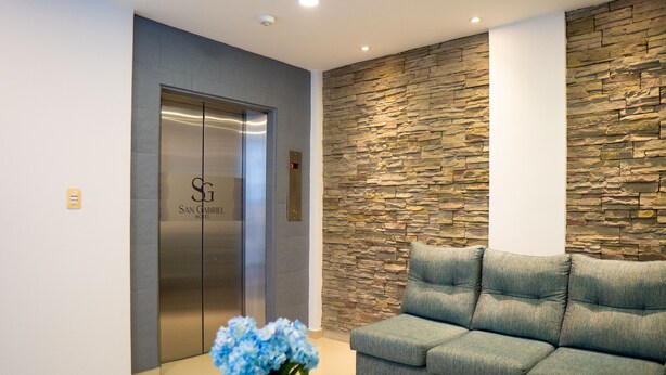 A reception area with a stone wall, a grey sofa, and an elevator with a logo. - Hotel San Gabriel (Barrancabermeja)