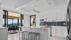 A modern kitchen with white cabinetry, a central island with bar stools, a microwave, and a view of the ocean.