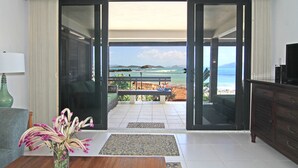 A living room with a view of the beach, a sofa, a coffee table, and a TV.