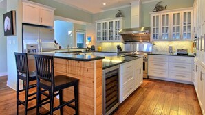 Une cuisine moderne avec des meubles blancs, un réfrigérateur en acier inoxydable et un îlot central en bois doté de tabourets de bar.