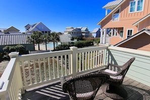 A wooden deck with wicker chairs and a white fence. - Stunner w/ Wrap-Around Porch in Cinnamon Shore, by Dune Crossover (Port Aransas)