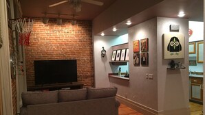 Una sala de estar con pared de ladrillo, un televisor de pantalla plana, un sofá y un ventilador de techo.