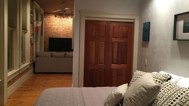 Una habitación con cama, sofá, pared de ladrillo, puerta de madera y ventilador de techo.