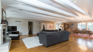 A spacious living area with a grey sofa, wooden flooring, a white rug, and a dining area with wooden chairs and a table.