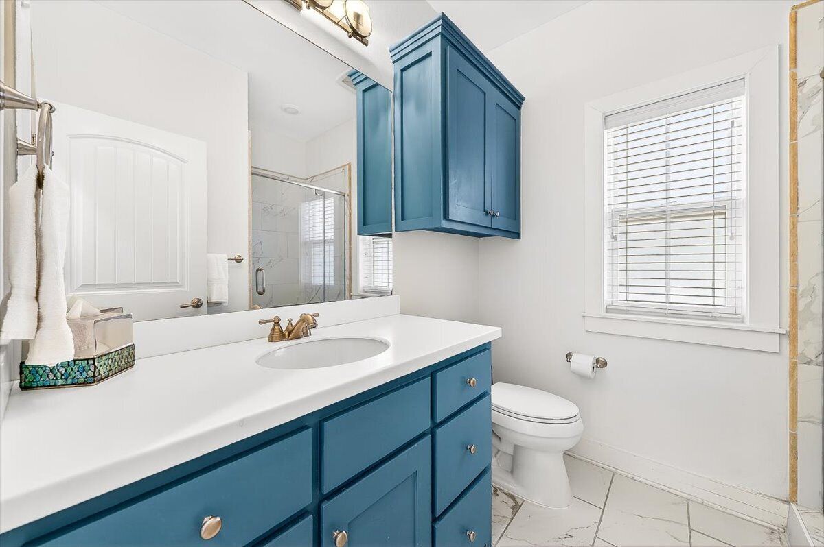 Une salle de bain avec un lavabo blanc, des meubles bleus, des toilettes blanches et un grand miroir.