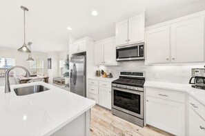 A modern kitchen with white cabinets, stainless steel appliances, and a marble countertop.