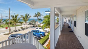 A covered balcony with a view of parked cars and palm trees, leading to a building with windows. - Beachfront Bliss – Anna Maria Island #11 RVA (Bradenton Beach)