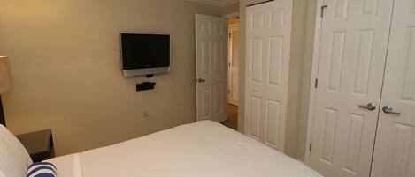 A hotel room with a bed, a ceiling fan, a TV mounted on the wall, and white doors.