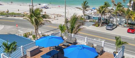 A rooftop patio with outdoor seating and umbrellas overlooking a beach.