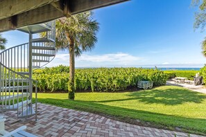 A spiral staircase leading to a covered area with a view of a well-maintained lawn and a distant body of water.
