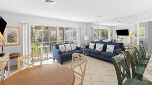 A spacious living room with a large dining table, two sofas with patterned cushions, and a TV mounted on the wall. - Charming 2BR Condo Outrigger #4  by RVA (Longboat Key)