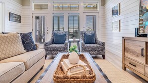 A cozy living room with a sofa, two patterned armchairs, a coffee table with books and a vase, and a wooden cabinet. - Custom, Designer Condo w/ Luxe Interiors+Enviable Amenities@Cinnamon Shore! (Port Aransas)