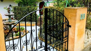 A gated entrance with a decorative fountain, a house with a tiled roof, and a number plaque.