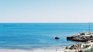 A coastal scene with clear blue water, rocky shoreline, and a few boats in the distance.