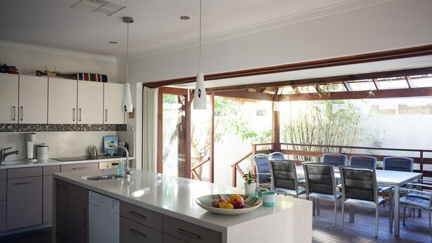 A modern kitchen with a large island, a dining area with outdoor seating, and a view of bamboo trees.