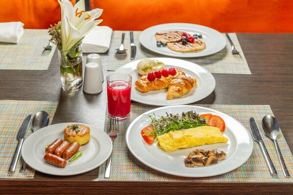 A breakfast setting with plates of food, a glass of red juice, and a vase with flowers. - Hyatt Place Riyadh Al Sulaimania (Riyadh)