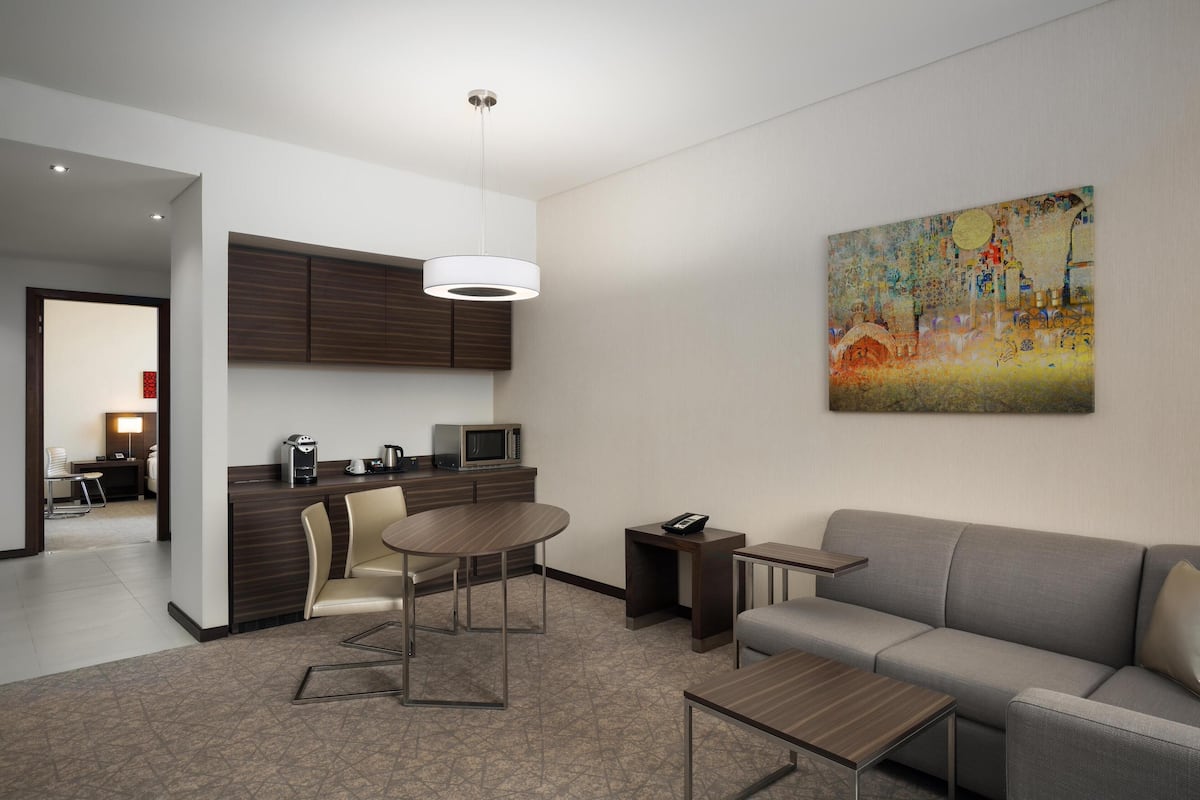 A modern hotel room with a dining area, a sofa, a painting, and a kitchenette.