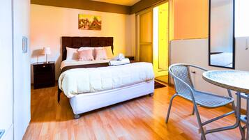 Habitación de hotel con cama, mesita de noche, una silla, una mesa y un cuadro en la pared.