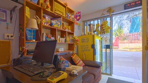 A reception desk with a computer, phone, and various items. There are shelves with snacks and a yellow vending machine. - Hermoza House Bed & Breakfast (Cusco)