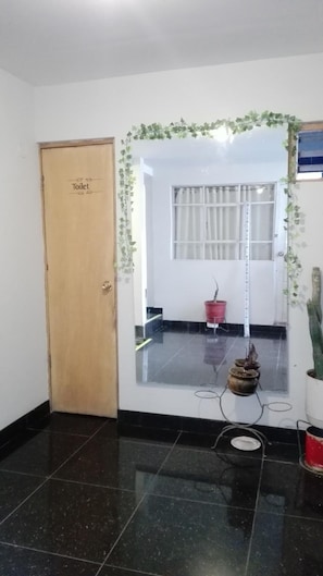 A hallway with a wooden door labeled 'Toilet,' a window with curtains, a potted plant, and a red bucket. - Hermoza House Bed & Breakfast (Cusco)