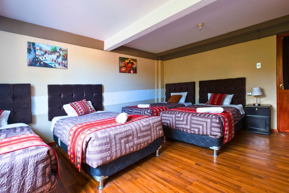 A hotel room with three beds, wooden flooring, and artwork on the walls.