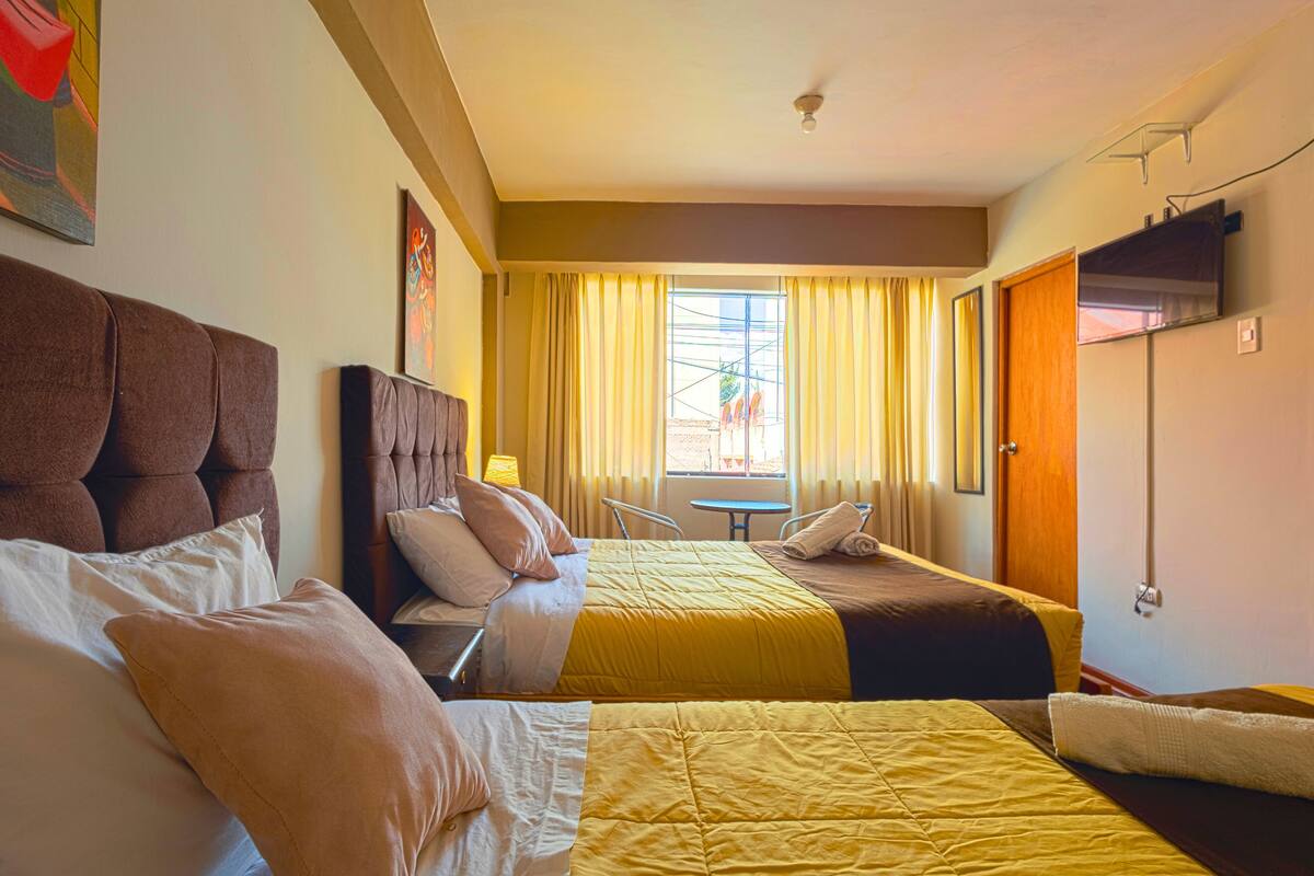 A hotel room with two beds, a small table, and a TV.
