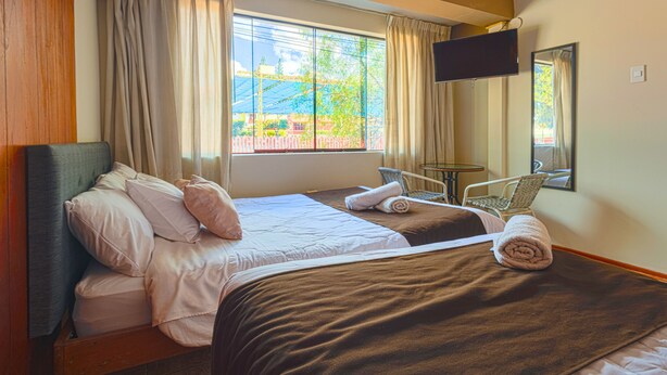 A hotel room with two beds, a TV, a small table, and a chair. - Hermoza House Bed & Breakfast (Cusco)