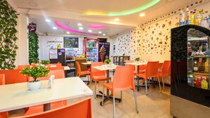 A restaurant with orange chairs and tables, a vending machine, and a wall decorated with food illustrations. - Hermoza House Bed & Breakfast (Cusco)