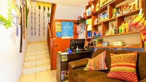 A cozy living room with a brown leather sofa, a desk with a computer, and shelves stocked with snacks and beverages. - Hermoza House Bed & Breakfast (Cusco)