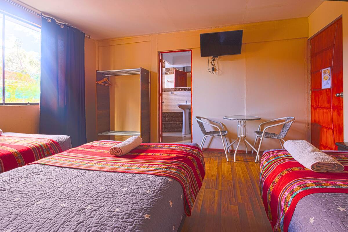 A hotel room with two beds, a desk, a chair, a TV, and a bathroom visible through an open door.