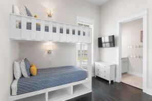 A bunk bed with a striped mattress, a white bedside table, a wall-mounted TV, and a coat rack. - Charming Home in Cinnamon Shore w/ Access to Many Resort-Like Amenities (Port Aransas)