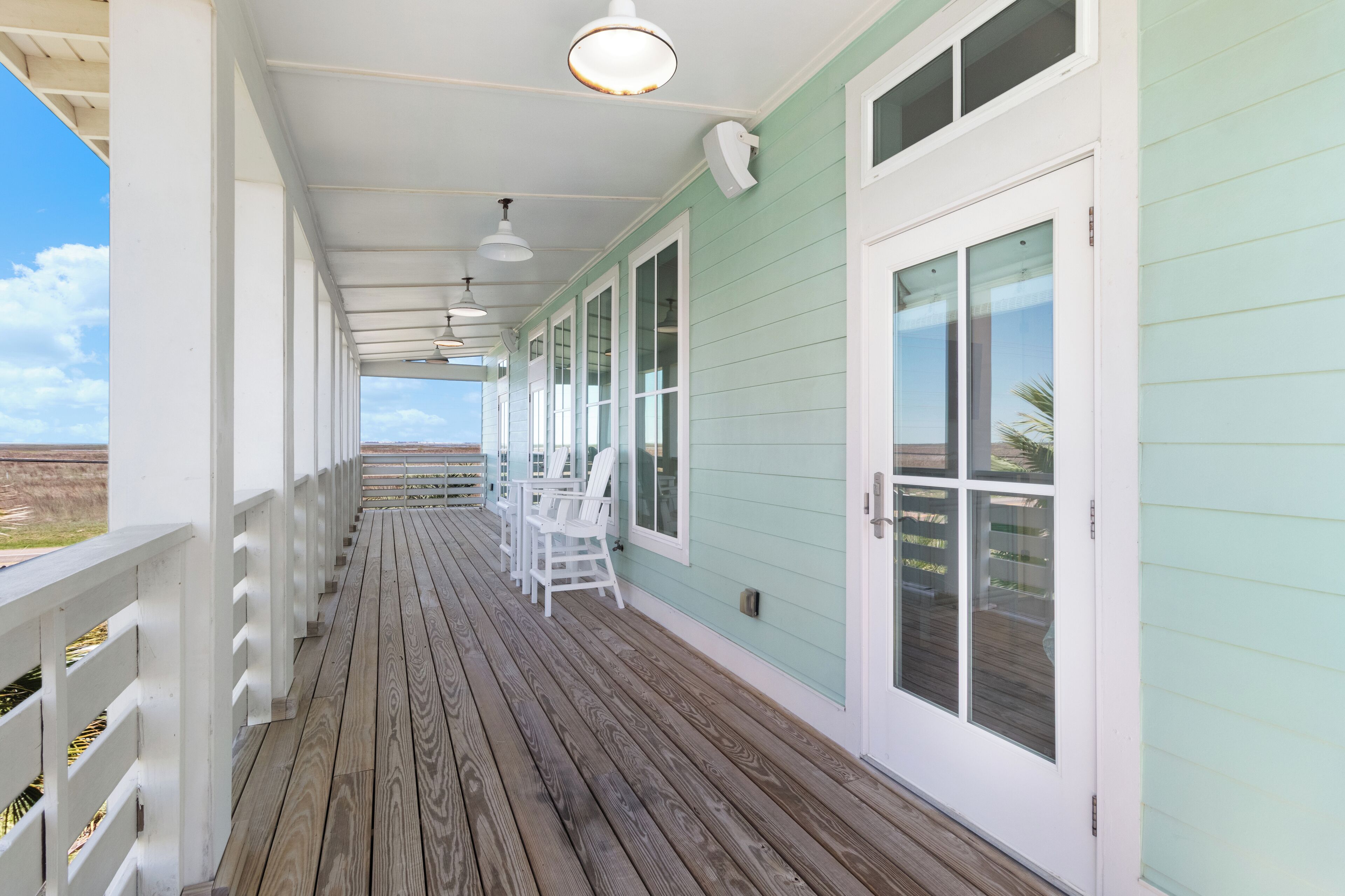 Une terrasse en bois couverte, dotée de rampes blanches et d’un mur extérieur de couleur vert clair.