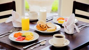 Une table mise pour le petit-déjeuner avec des assiettes de fruits, des viennoiseries, un verre de jus d’orange, une tasse de café et une bouteille de lait.