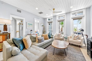 A spacious living room with a large sofa, a coffee table, and a dining area with a lamp.