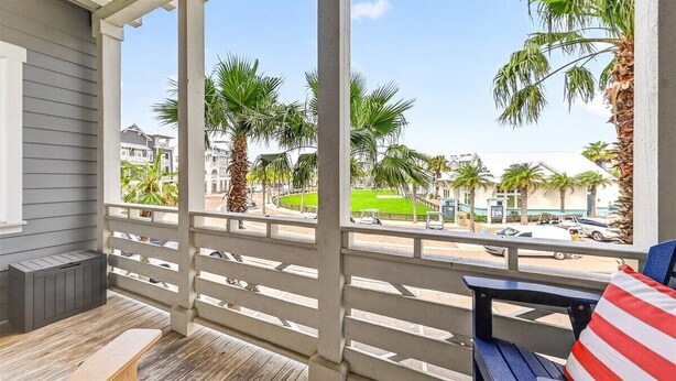 A covered outdoor seating area with a view of palm trees and buildings. - Come stay with us at the Golden Hour! Spacious and relaxing 2 bed/2 bath cond (Port Aransas)