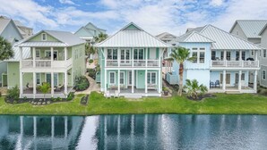 A row of coastal homes with balconies, a grassy lawn, and a body of water in the foreground. - Pet-Friendly, Lakeside Home at Cinnamon Shore w/ Access to Pools & More (Port Aransas)