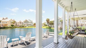 A covered outdoor area with white chairs and a hanging hammock overlooking a body of water and buildings. - Pet-Friendly, Lakeside Home at Cinnamon Shore w/ Access to Pools & More (Port Aransas)