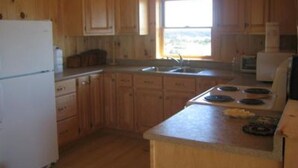 A kitchen with wooden cabinets, a refrigerator, a sink, and a window. - New Log Home with Gorgeous Ocean View in Historic Acadian Village (L'Ardoise)