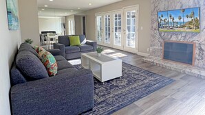 A spacious living room with a gray sofa, a white coffee table, and a blue rug. There is a fireplace with a TV mounted above it. - **Water Slide!**Pool**Spa**Game Room!! (Anaheim)