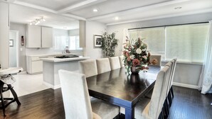 A dining area with a large table, chairs, and a vase of flowers. There is a kitchen in the background with white cabinets and a window with blinds. - **Water Slide!**Pool**Spa**Game Room!! (Anaheim)