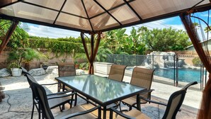 An outdoor patio with a glass table and chairs, a large umbrella, and a view of a swimming pool and waterfall. - **Water Slide!**Pool**Spa**Game Room!! (Anaheim)