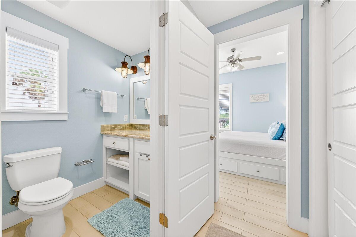 Ein Badezimmer mit Toilette, Waschbecken, Spiegel, Handtuchhalter und Deckenventilator.