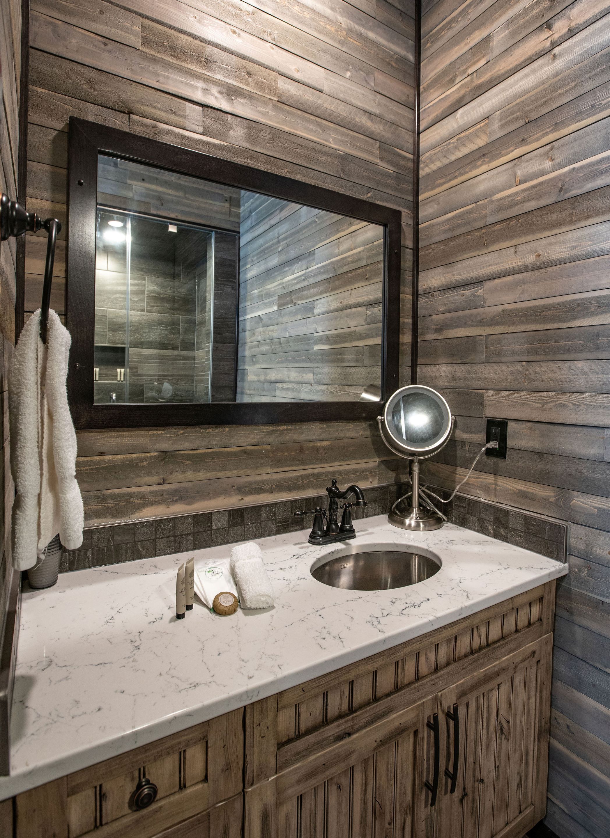 Un baño con pared de madera, un espejo, un lavamanos con encimera de mármol y un perchero para toallas.