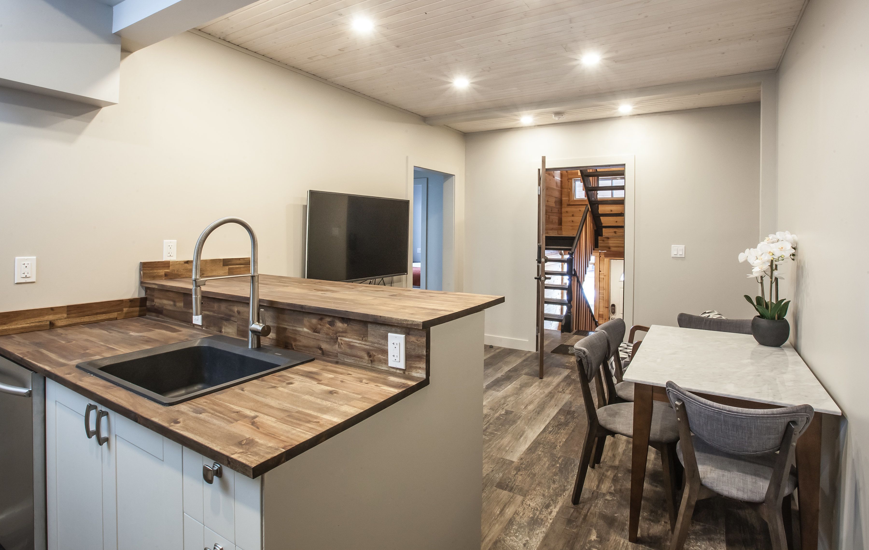 Una cocina moderna con encimera de madera, un fregadero y una televisión integrada. Hay una zona de comedor con una mesa y sillas.