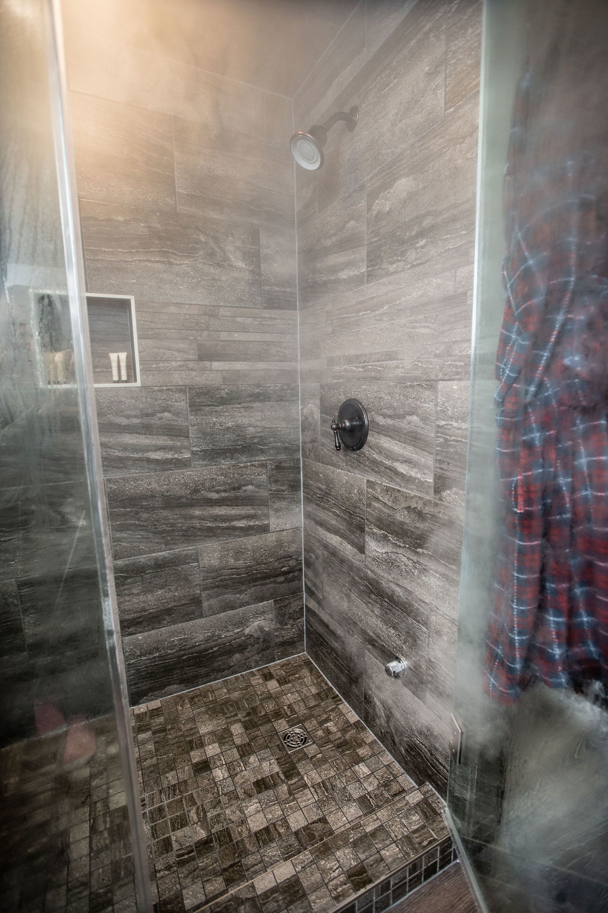 A shower with a glass door, a showerhead, and a tiled floor.