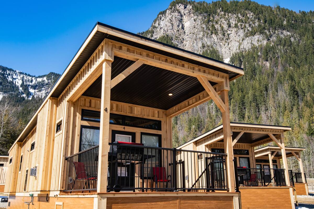 A wooden cabin with a balcony, a covered patio, and a mountain backdrop.