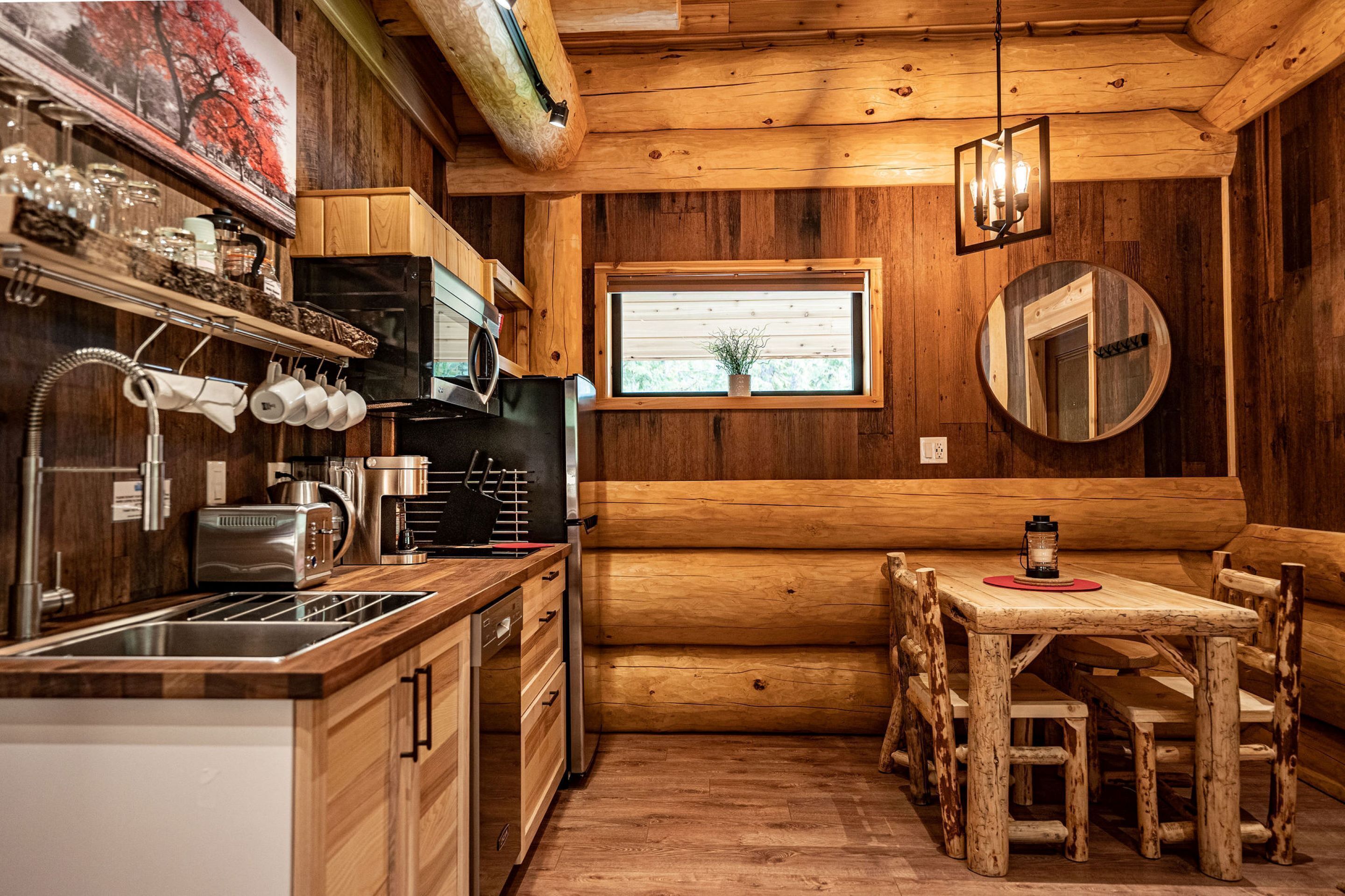 Interior de una cabaña de madera con cocina, comedor y ventana con vistas.
