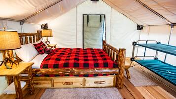A tented room with a wooden bed, a small table with a lamp, and a bunk bed.